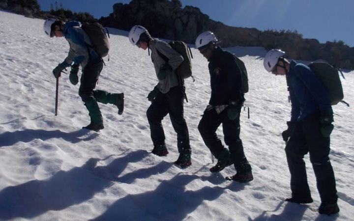 A group of outward bound students wearing mountaineering gear make their way up a snowy incline. 